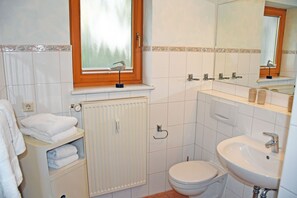 A bathroom with a window, a radiator, a toilet, a sink, and a towel rack.