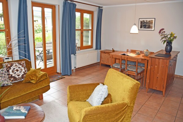 A cozy living room with a yellow armchair, a wooden dining table, and a blue curtain-covered window.