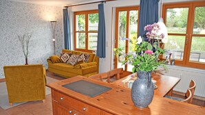 Ein gemütliches Wohnzimmer mit einem Holzesstisch, einer Couch mit gemusterten Kissen und einer Vase mit Blumen.