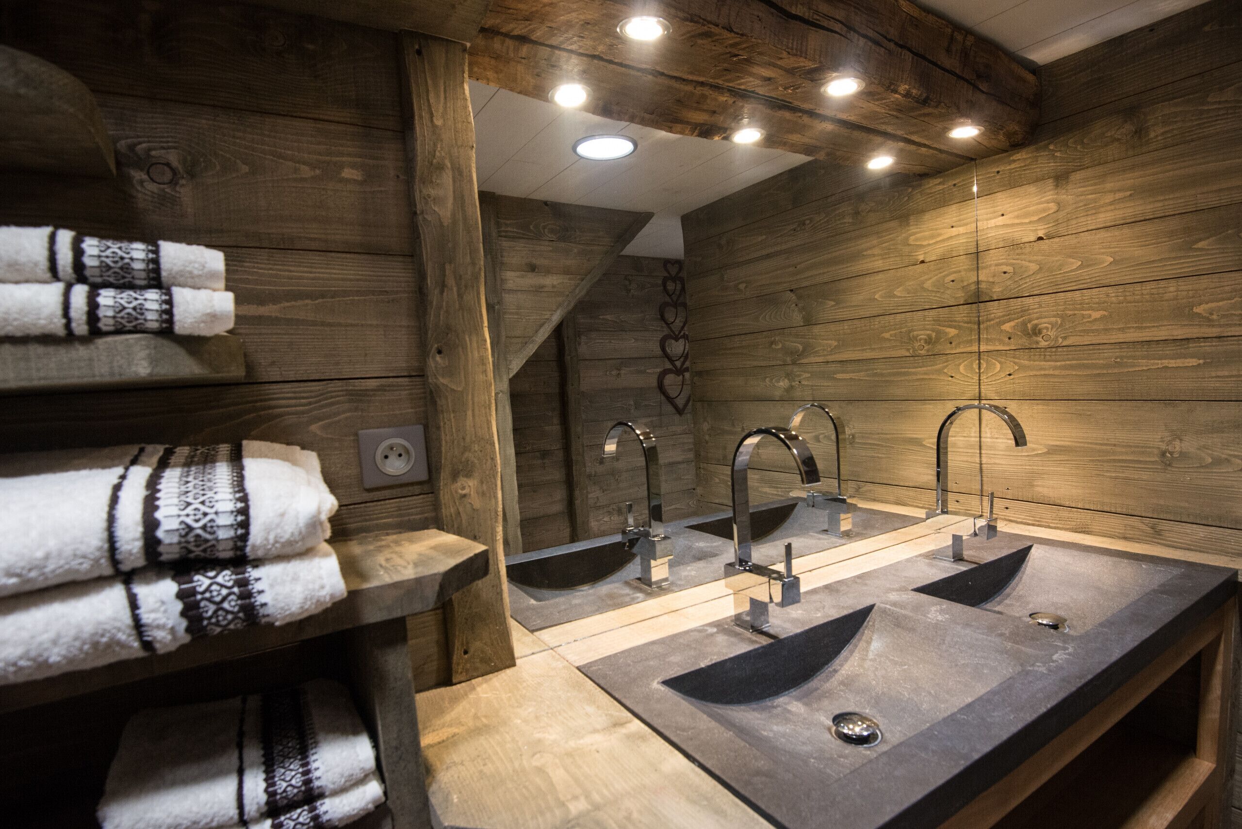 A bathroom with wooden walls, three sinks, and towels on a shelf.
