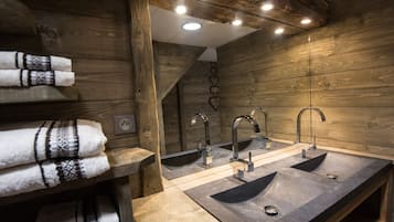 A bathroom with wooden walls, three sinks, and towels on a shelf.