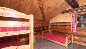 Une pièce de cabane en bois avec des lits superposés, une fenêtre avec des rideaux et un mur en rondins.