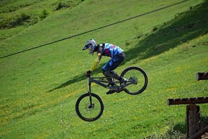 A person on a mountain bike performing a jump over a wooden obstacle in a grassy field.