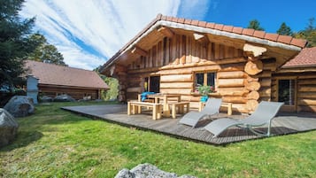 Una cabaña de troncos con un porche de madera, mobiliario exterior y vistas del paisaje circundante.