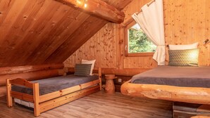 Een slaapkamer in een blokhut met twee bedden, een raam met gordijnen en een houten plafond.