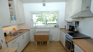 A compact kitchen with a wooden table, white cabinets, a window, and a dishwasher.