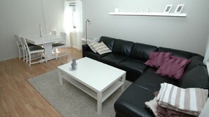 A modern living room with a white coffee table, black leather sofa, and a dining area with a white table and chairs.