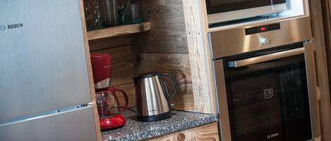 Cocina compacta con refrigerador Bosch, microondas, cafetera y hervidor sobre encimera de madera.