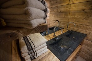 A wooden cabin interior with a black sink, two faucets, and a towel rack with folded towels.