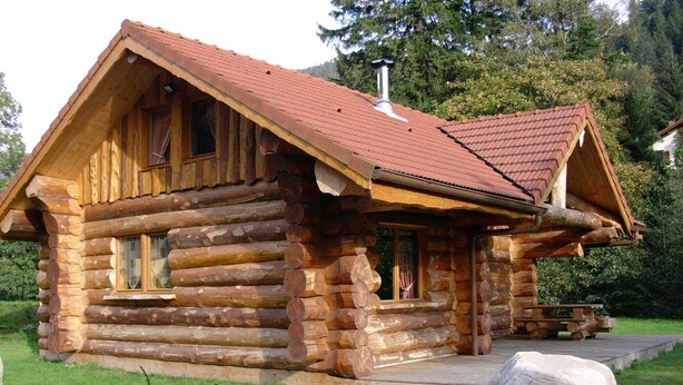 Une cabane en rondins avec un toit rouge, un revêtement extérieur en bois et une véranda.