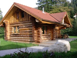 Une cabane en rondins avec un toit rouge, un revêtement extérieur en bois et une véranda.
