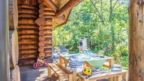 Une terrasse en bois avec des tables de pique-nique, un vélo pour enfants et un ballon de football.