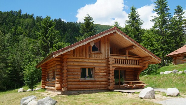 A log cabin with a balcony, a porch, and a small outdoor seating area.