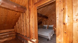 A wooden interior with a bed, pillows, and a nightstand.