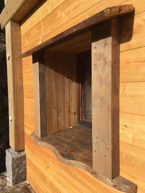Une cabane en bois dotée d’une grande fenêtre, de fondations en pierre et d’une porte en bois.