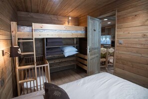 A wooden cabin room with bunk beds, a desk, and a chair.