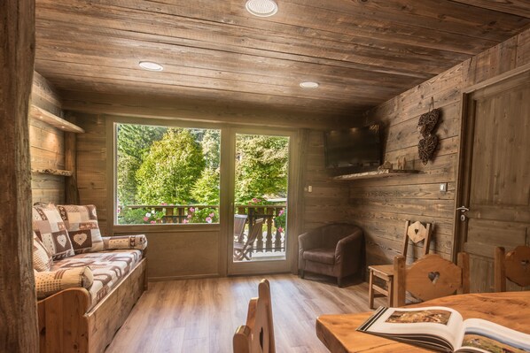 A wooden cabin interior with a sofa, chairs, a table, and a TV.