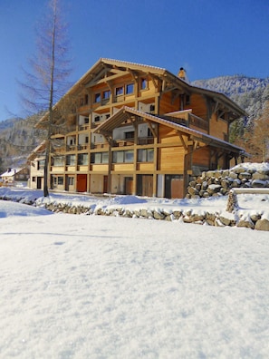 A multi-story wooden building with balconies, set against a snowy landscape with mountains in the background.