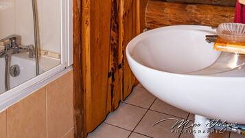 Een houten badkamer in een vakantiehuisje, met een douche, wastafel en raam.