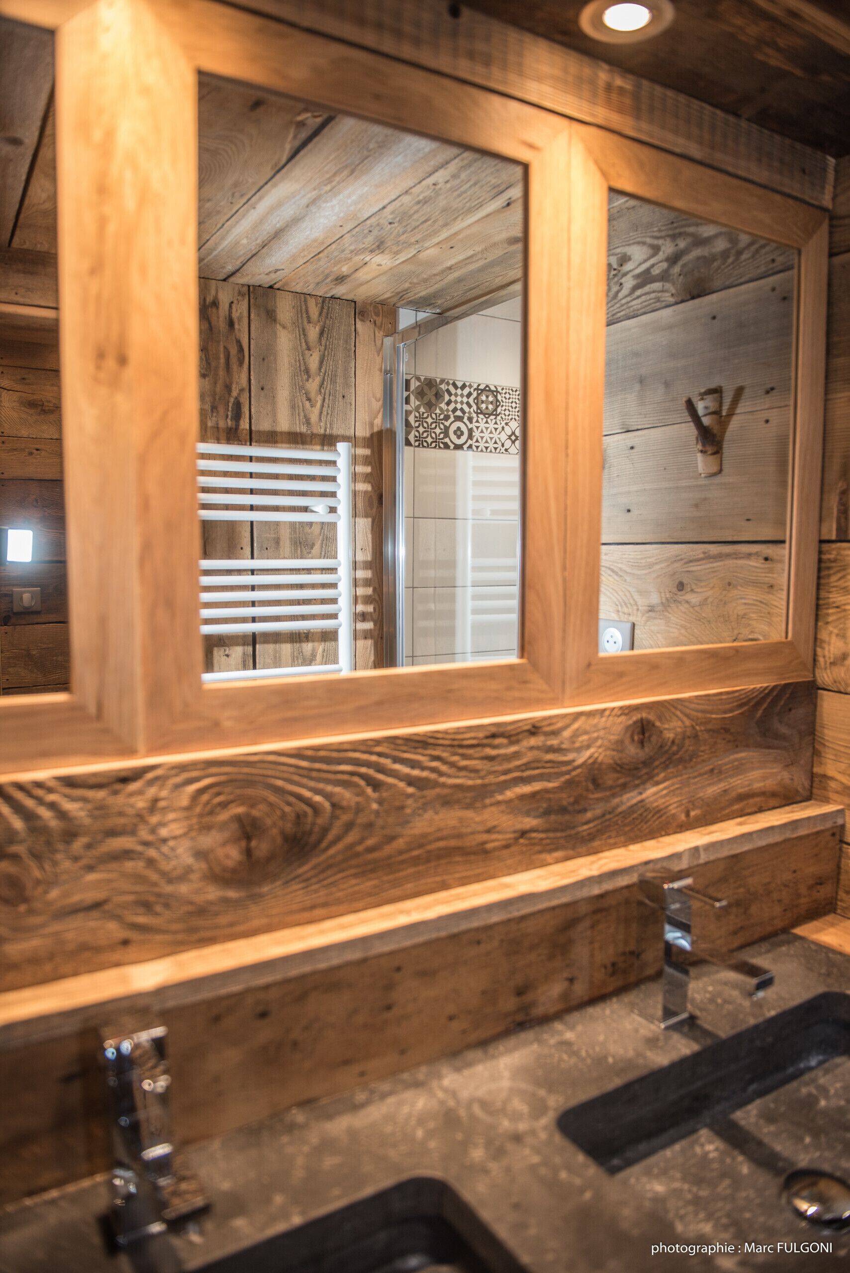 A wooden-framed mirror with a view of a bathroom vanity and a patterned tile backsplash.