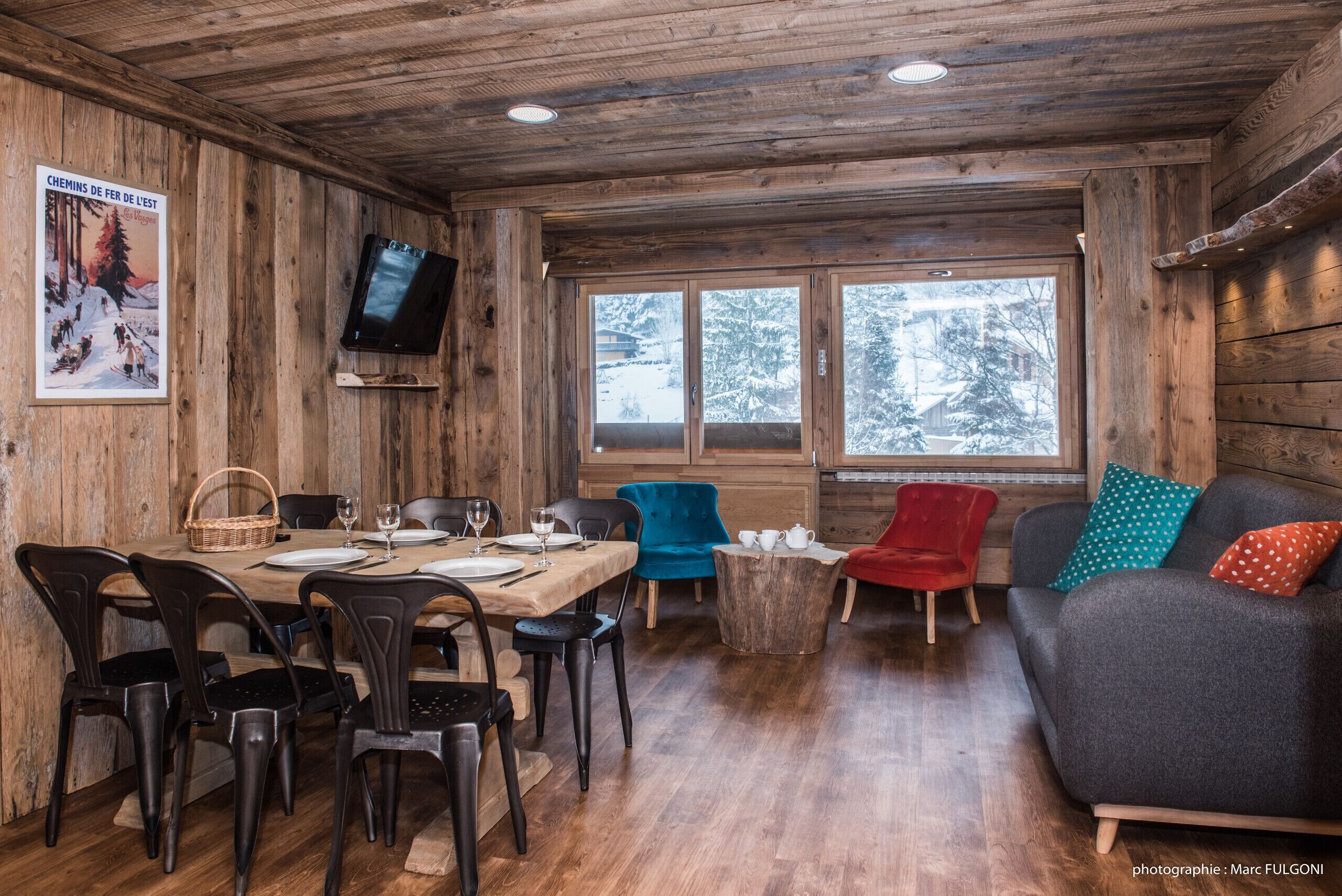 Un intérieur en bois comprenant une table à manger pour quatre personnes, un canapé et un téléviseur fixé au mur.