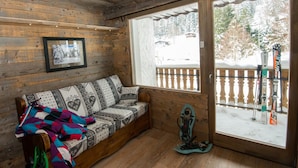 Een houten chalet met een bank, een ingelijste foto en een ski-rek naast een groot raam.