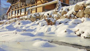 Een ruime houten chalet met meerdere balkons en een stenen steunmuur.