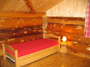Een kleine houten slaapkamer met een enkel bed, een nachtkastje met een lamp en houten wanden.