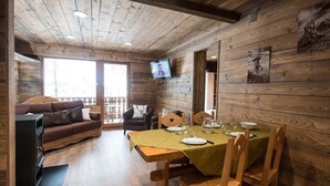 A wooden interior with a sofa, dining table, chairs, and a TV mounted on the wall. - Superbe appartement premium 42 m² La Bresse terrasse wifi vue montagne (La Bresse)