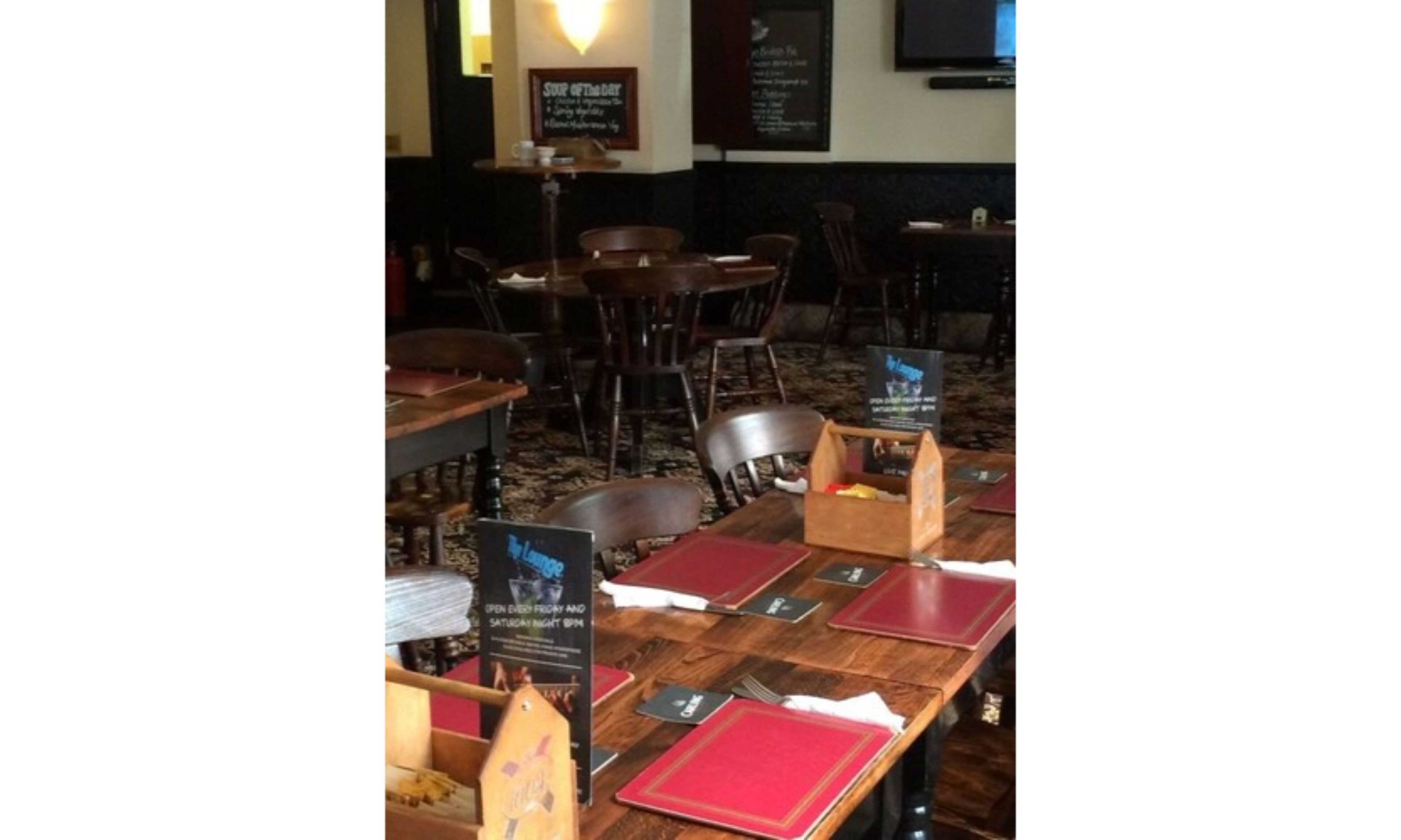 Un interior de restaurante con mesas y sillas de madera, una pizarra con el menú y un televisor colgado en la pared.