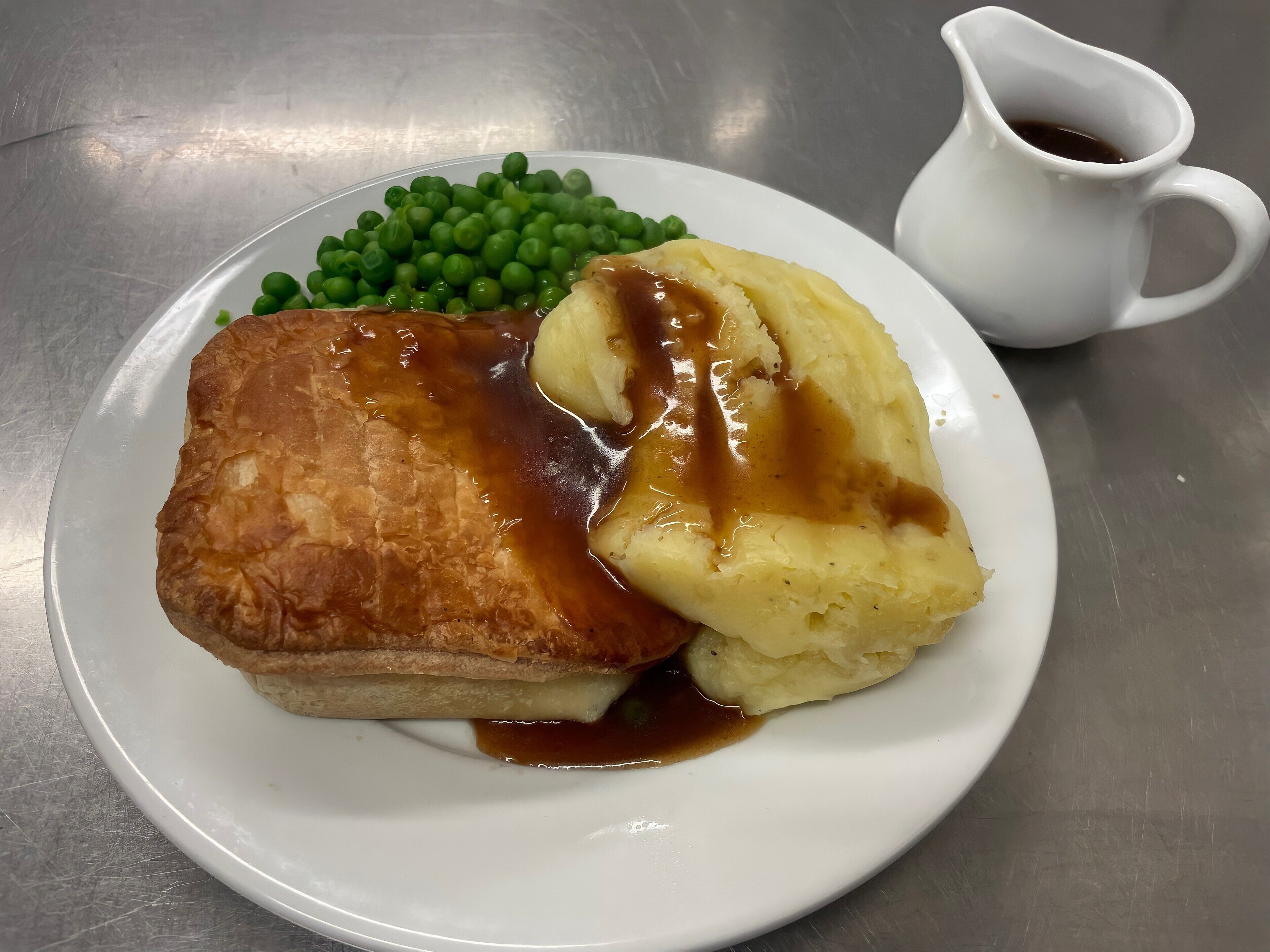Une assiette comprenant un Yorkshire pudding, de la purée de pommes de terre et des petits pois, accompagnée d'une saucière.