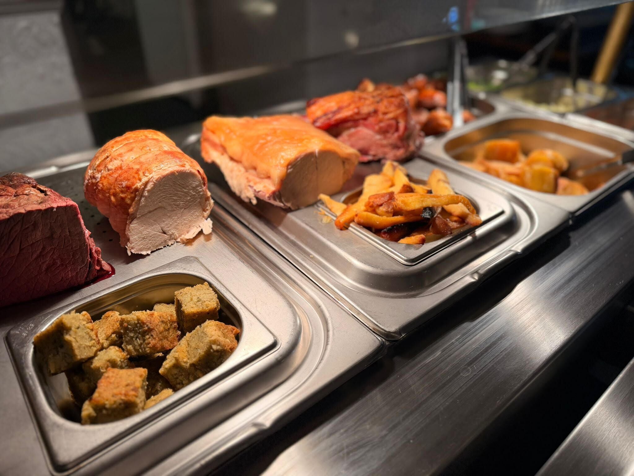 Un buffet proposant une variété de plats, notamment des viandes rôties, des frites et du pain.