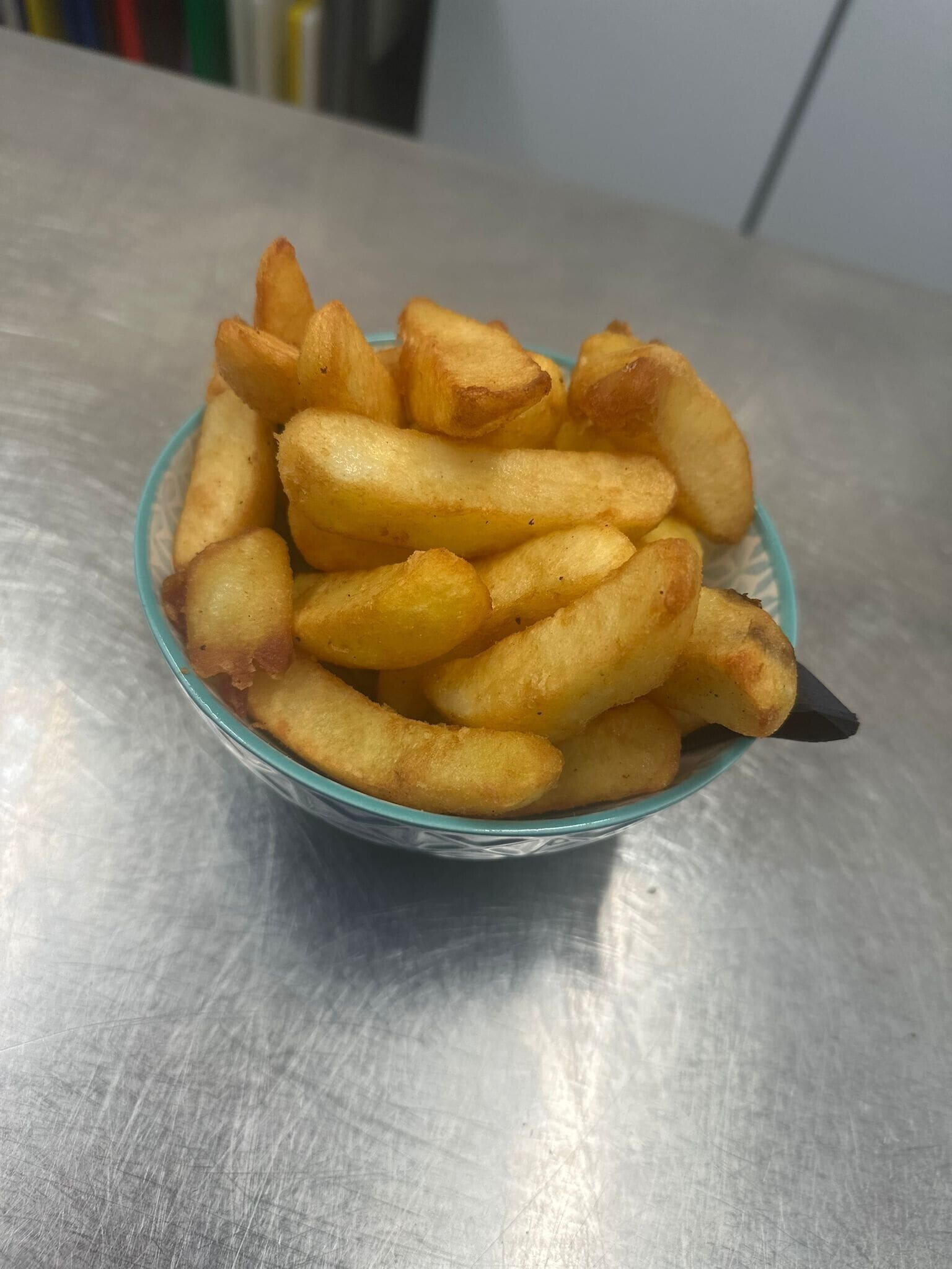 En skål med gyllenbruna pommes frites på en metallisk yta.