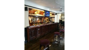 A bar area with wooden cabinets, a counter, and stools. - The Kings Arms (North Walsham)