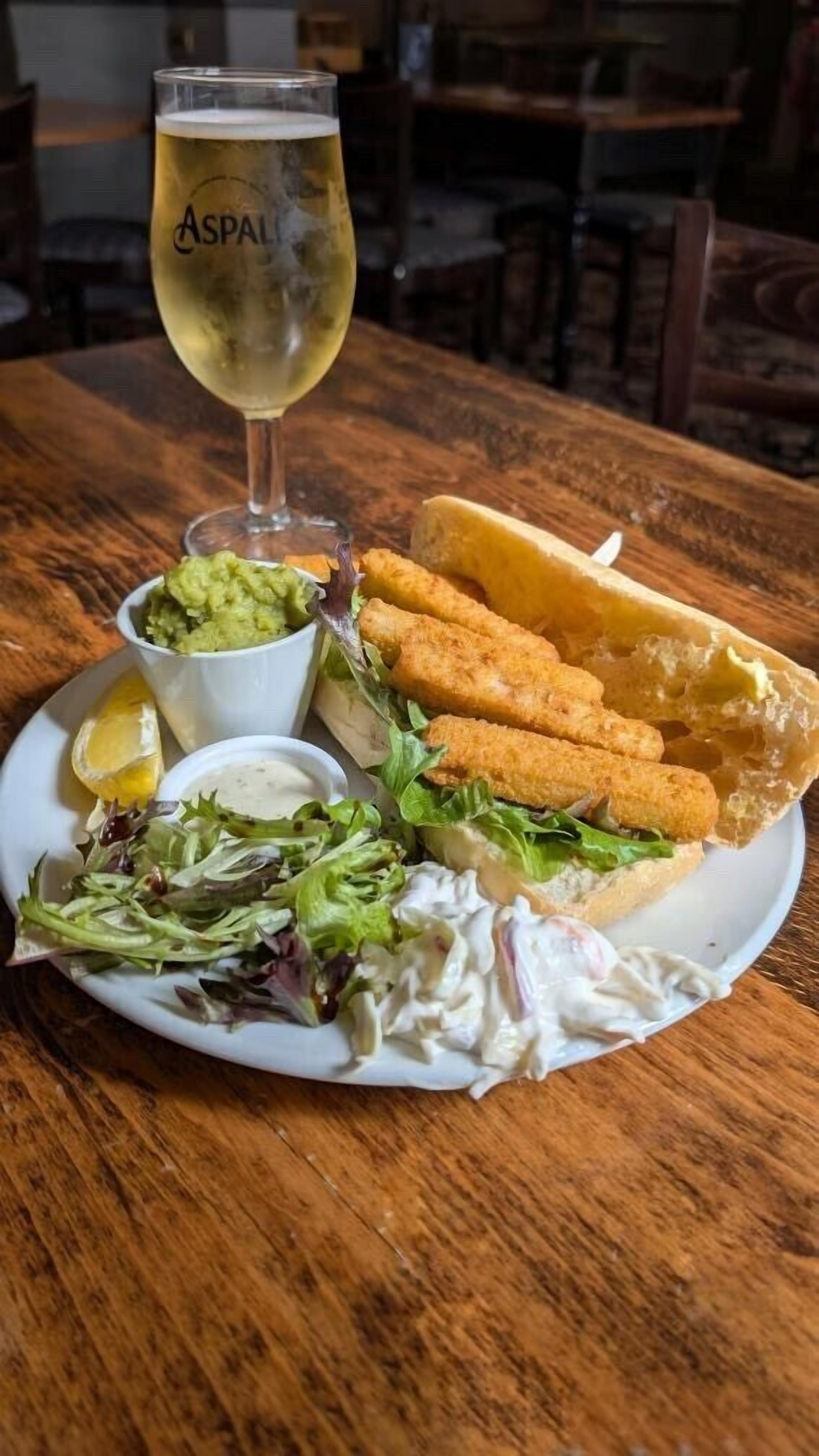 A meal consisting of breaded fish sticks, a salad, and a glass of white wine on a wooden table.