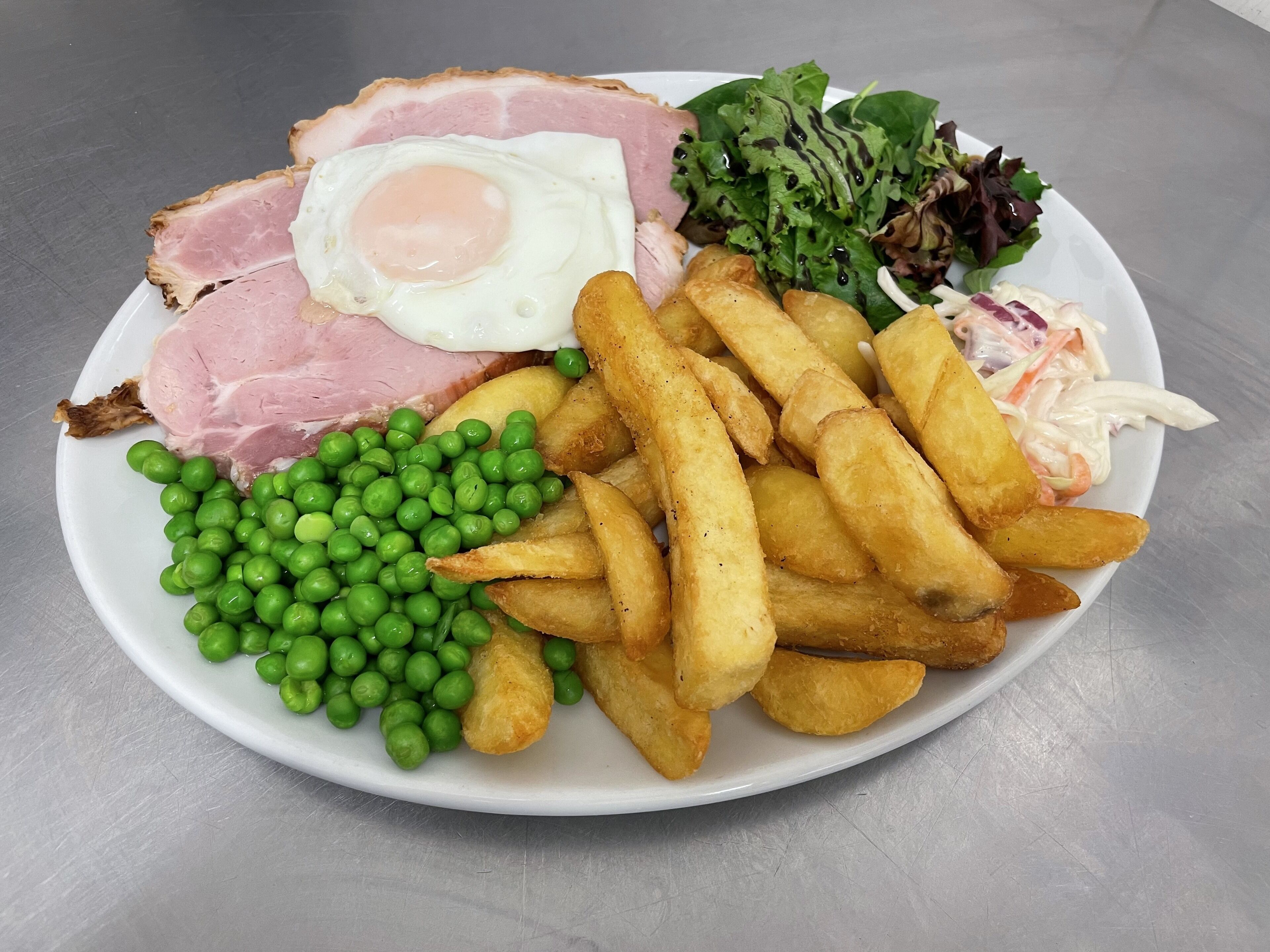 A plate with ham, fried egg, peas, fries, and salad.