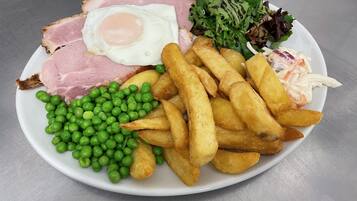 Un plato con jamón, huevo frito, guisantes, papas fritas y ensalada.