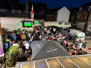 A crowded outdoor event with a large tent labeled 'THATCHERS' and a flag. - The Kings Arms (North Walsham)