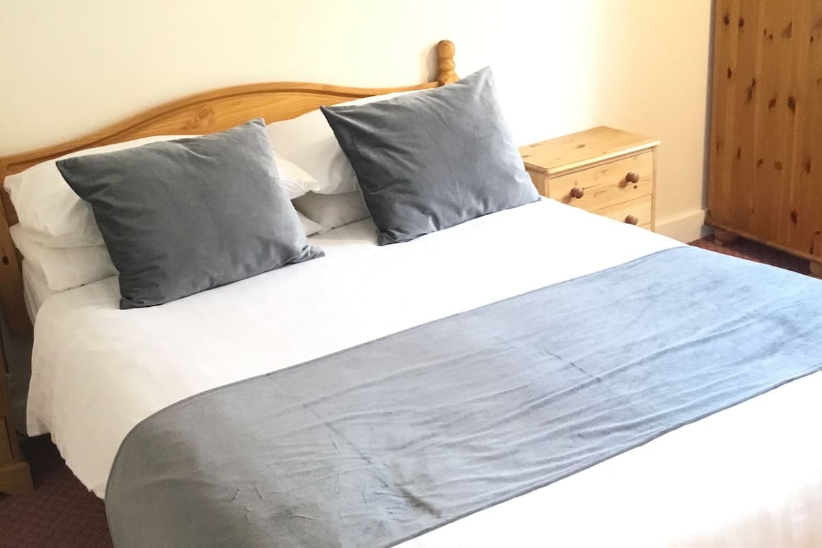 A neatly made bed with a wooden headboard, a grey blanket, and two grey pillows.