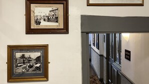 A hallway with framed black and white photographs on the wall, a sign indicating ladies and gentlemen, and a carpeted floor. - The Kings Arms (North Walsham)