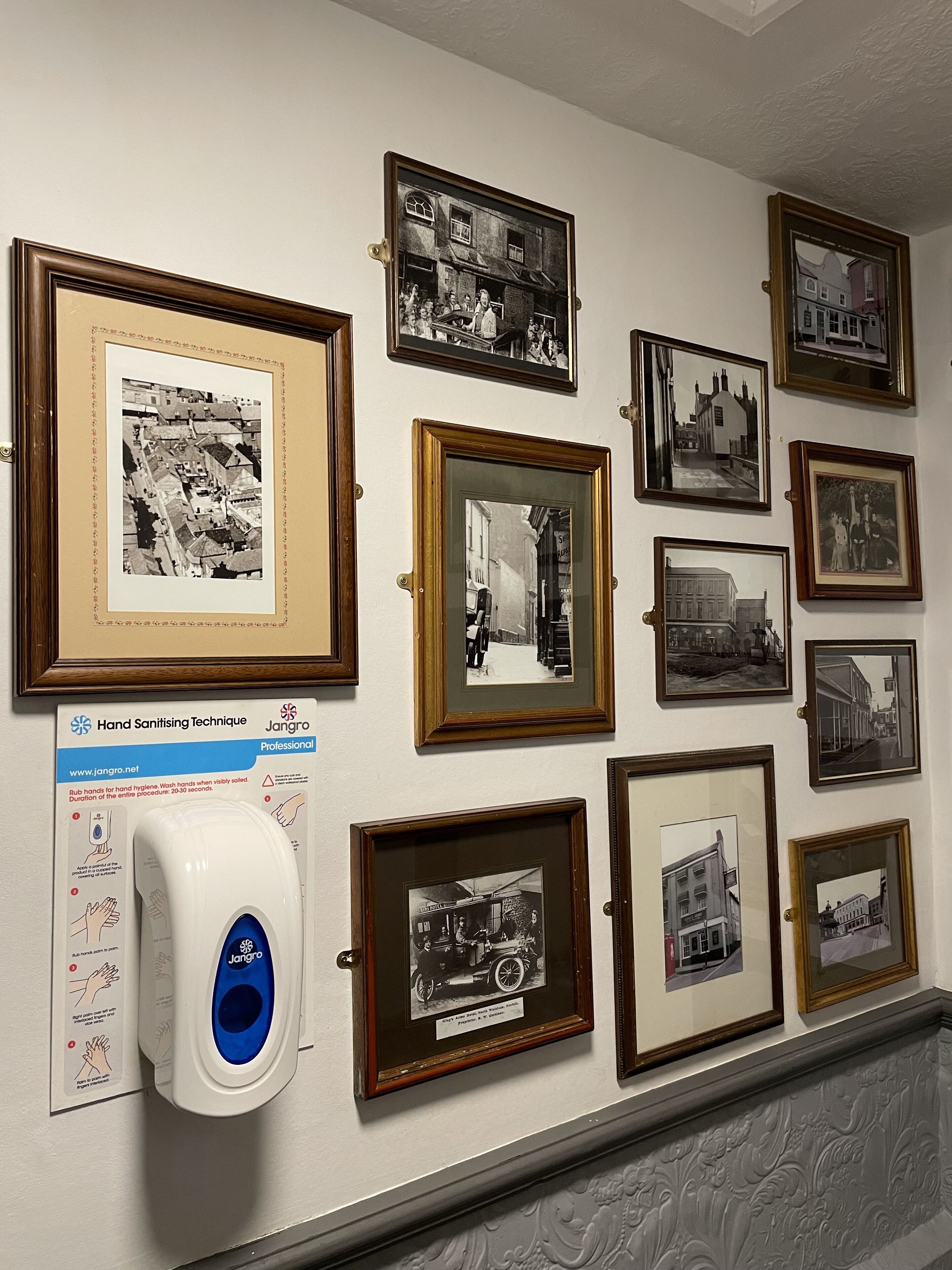Una pared con varias fotografías enmarcadas y un dispensador de gel antibacterial.