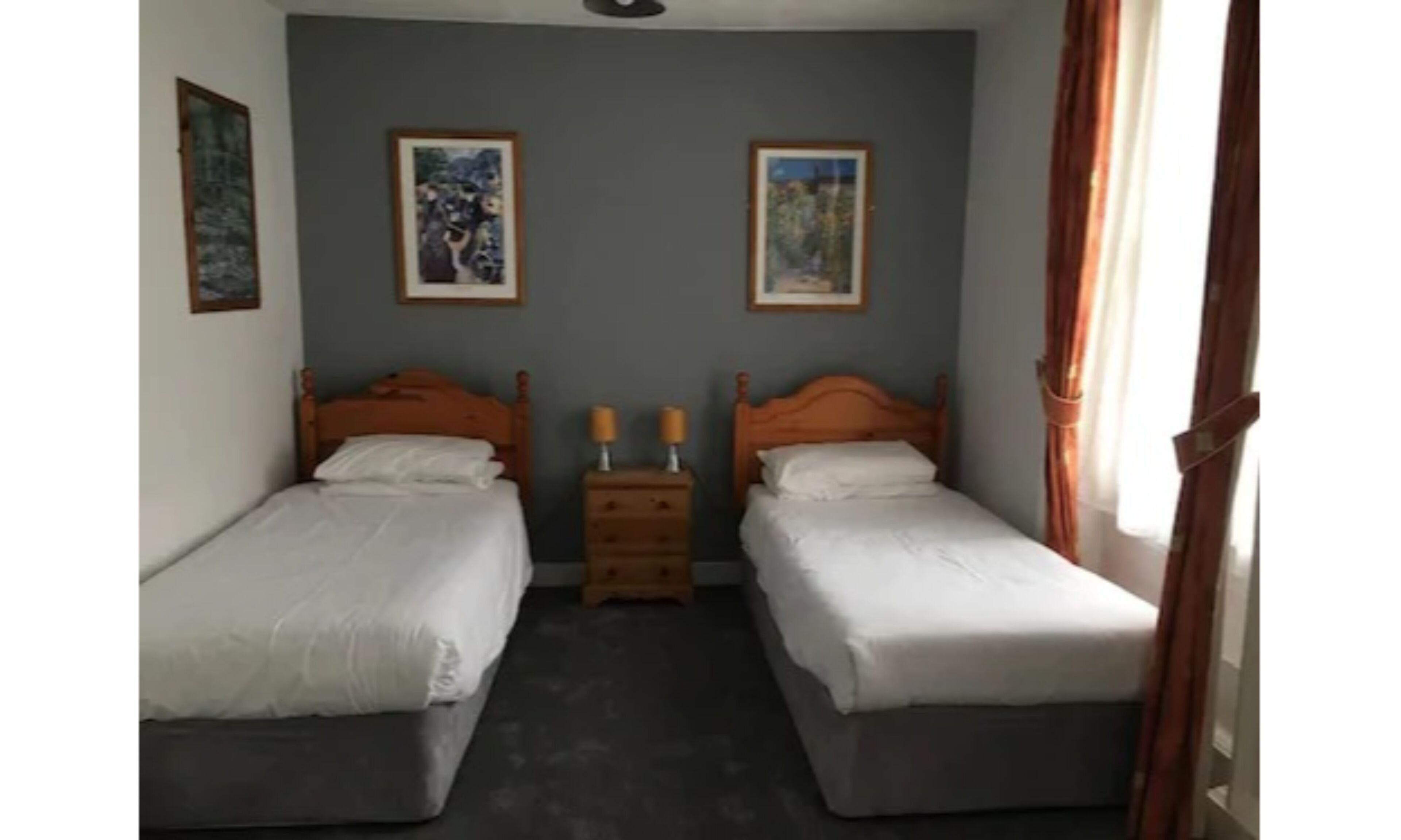A twin room with two single beds, a nightstand with two lamps, and two framed pictures on the wall.