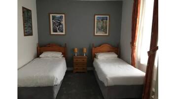 A twin room with two single beds, a nightstand with two lamps, and two framed pictures on the wall.