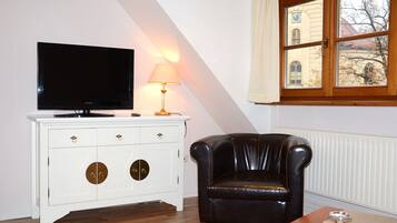 Una sala de estar con un televisor sobre un mueble blanco, un sillón de cuero y una ventana con vistas a un edificio.