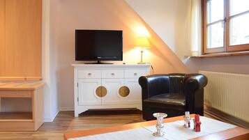 A room with a television on a white cabinet, a leather chair, a small table with a candle, and a window with a view.
