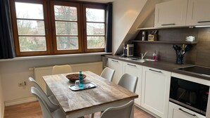 A modern kitchen with white cabinets, a wooden dining table, and a window with a view of buildings. - FRITZ Aparthotel Potsdam (Potsdam)