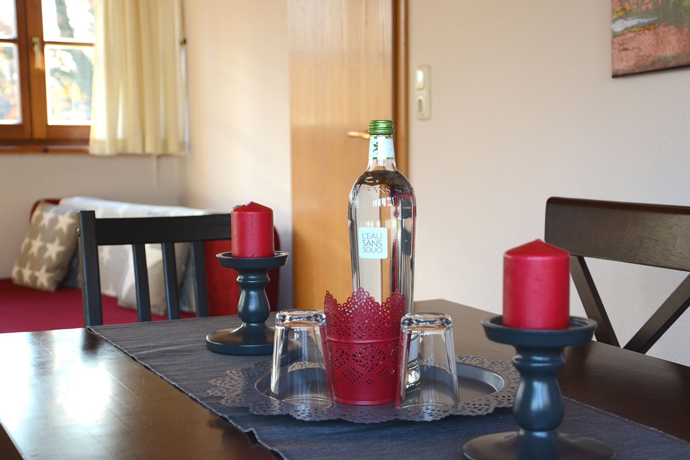 Een eettafel met een waterfles, rode kaarsen en zout- en peperstel op een placemat.