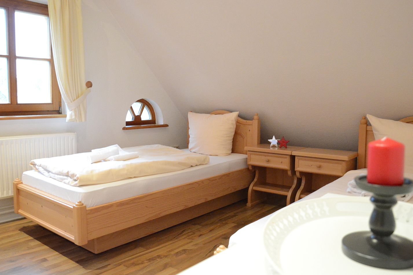 A bedroom with a wooden bed, a nightstand, a small table, and a window with curtains.