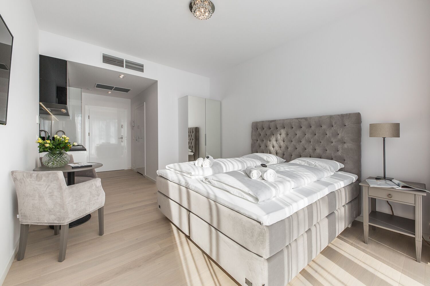 A modern bedroom with a large bed, a bedside table, a chair, a desk, and a mirror.