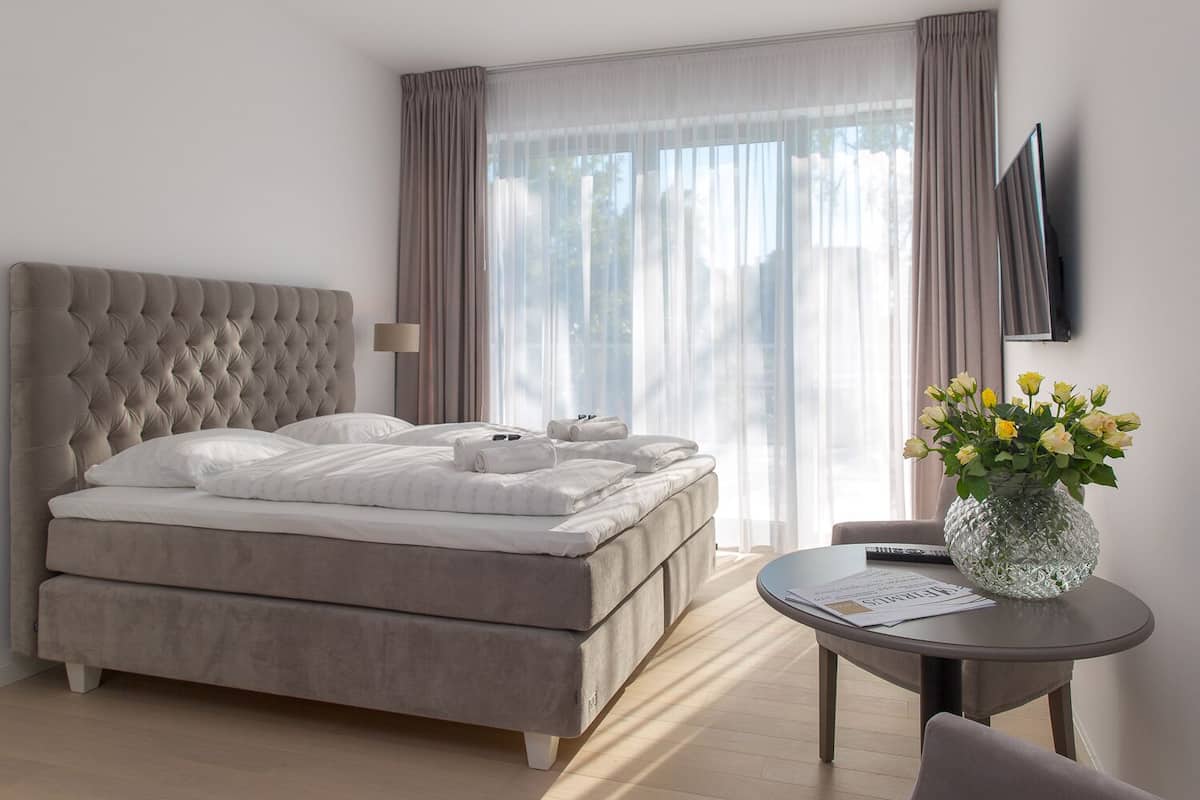 Quarto de hotel moderno com uma cama grande, uma mesa redonda e um vaso de flores.